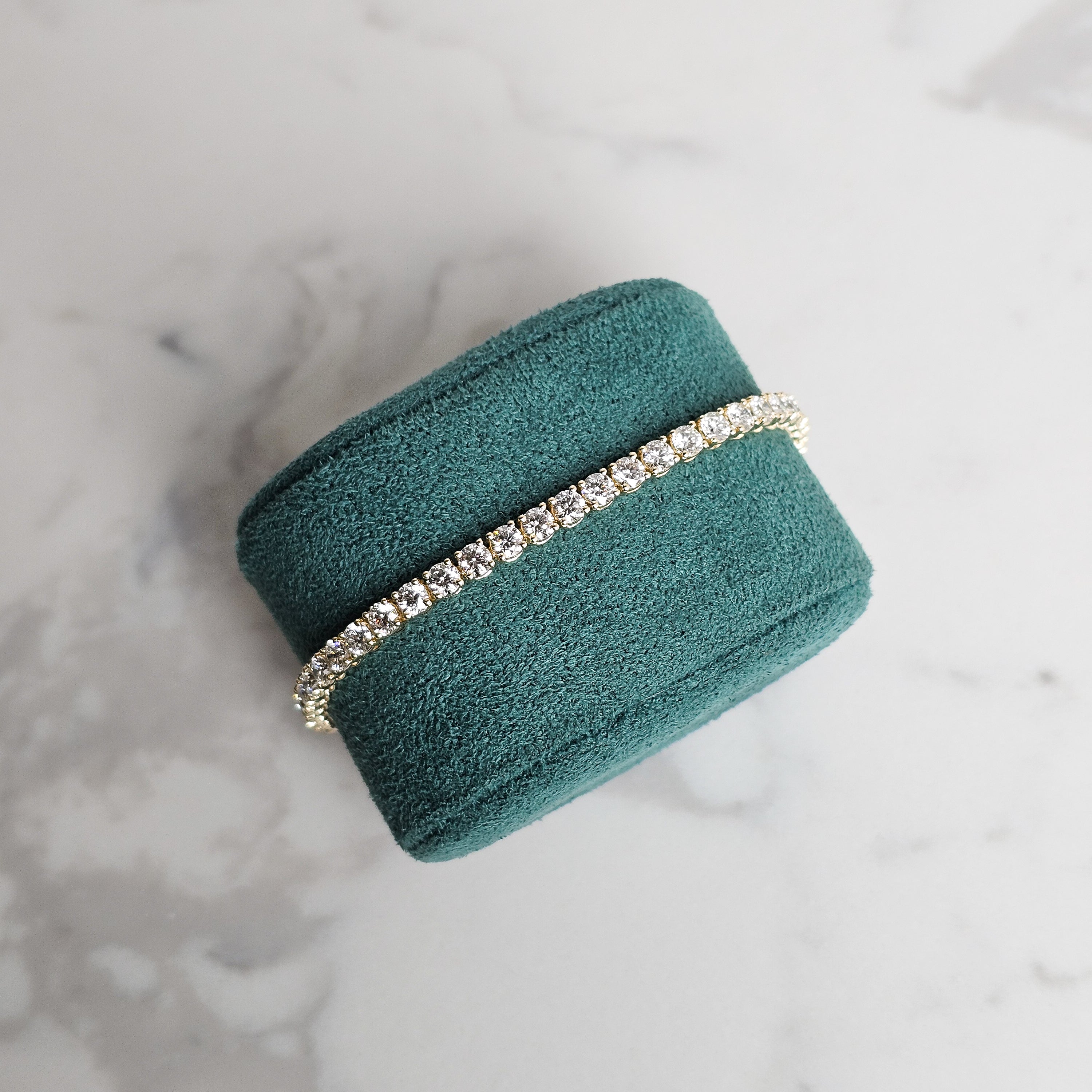 Yellow gold diamond tennis bracelet on marble background and green velvet jewellery display