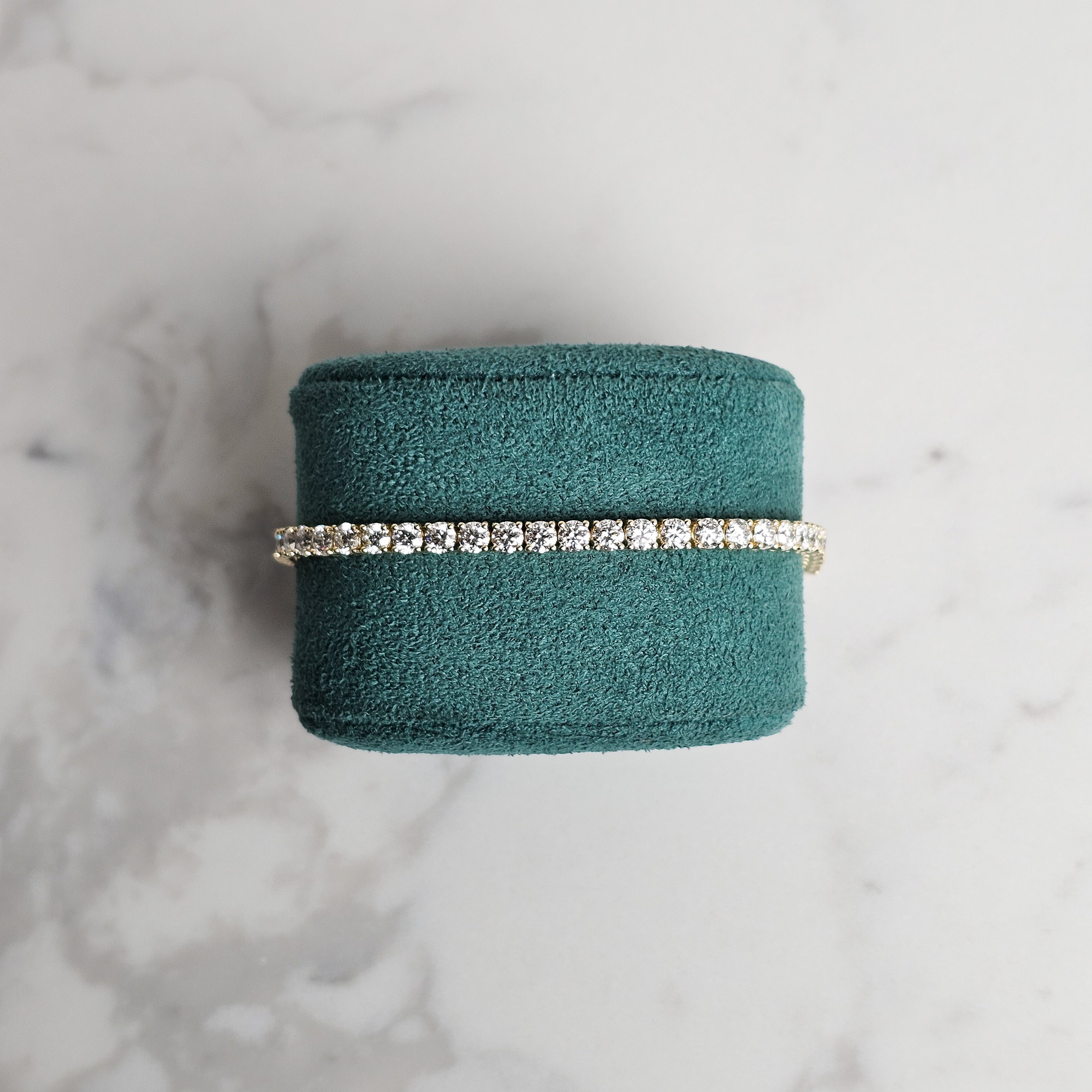 Yellow gold diamond tennis bracelet on marble background and green velvet jewellery display