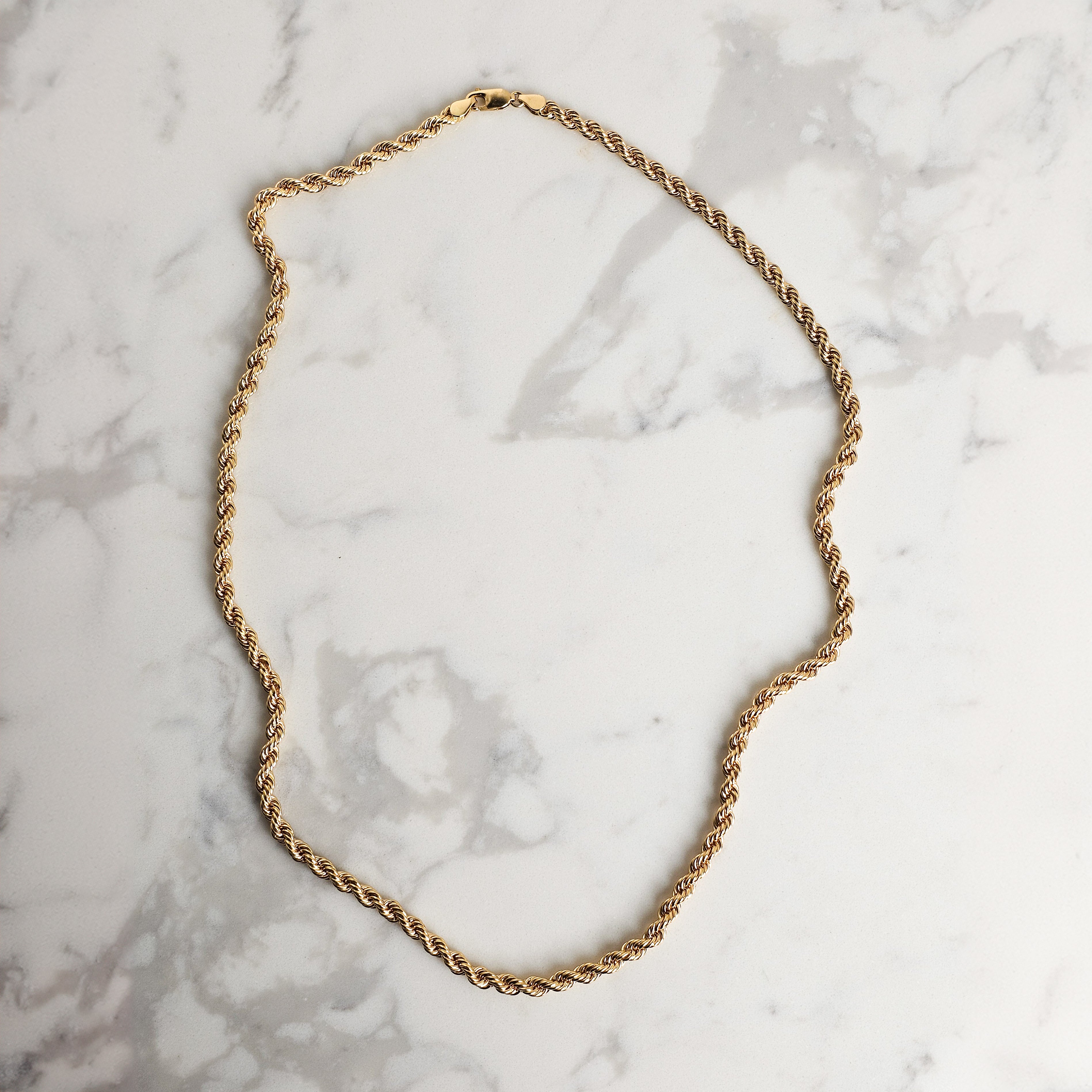mens rope chain in yellow gold on marble background artfully displayed