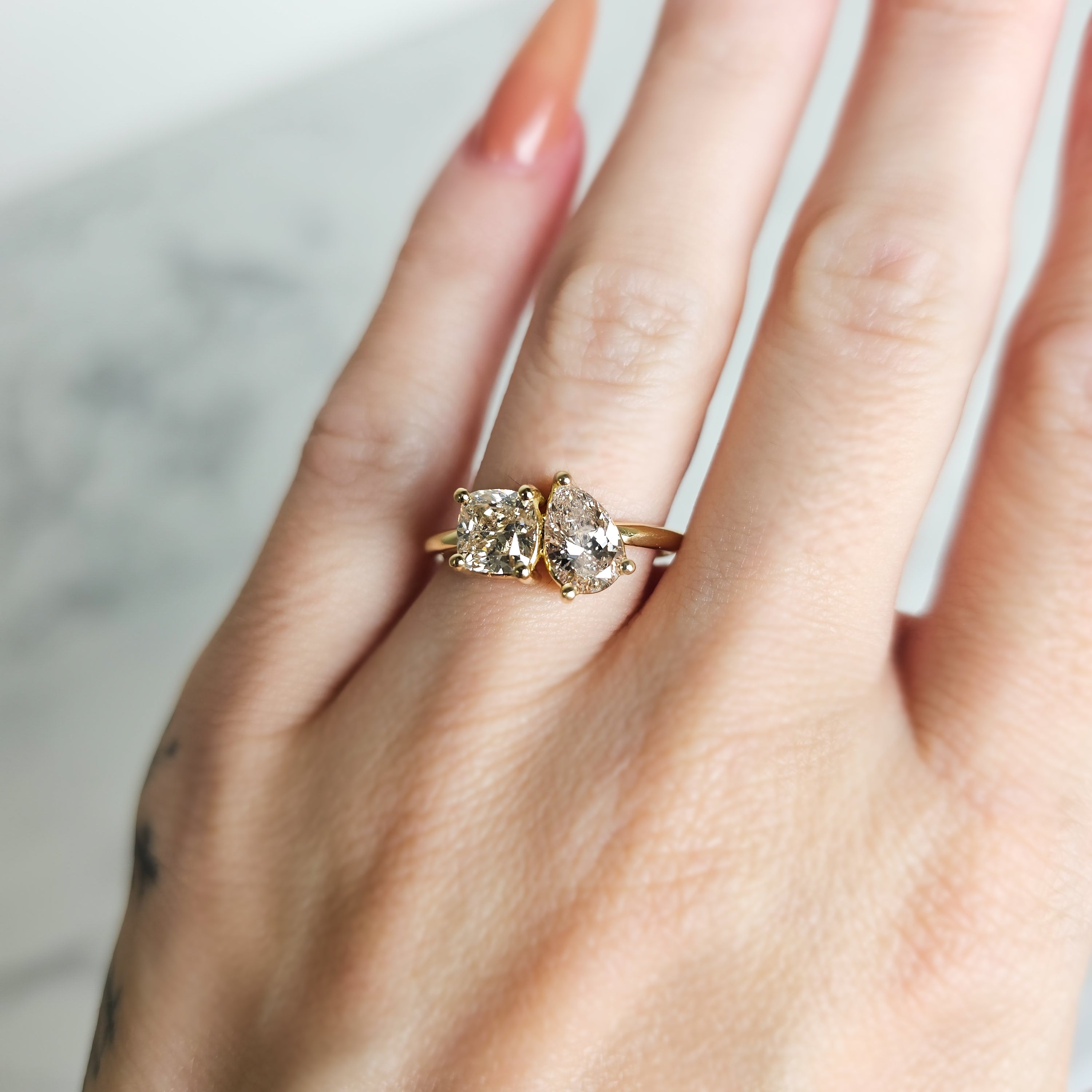 Hand wearing a Toi Et Moi Engagement ring in 18ct yellow gold featuring a cushion cut and fancy rear shape diamond