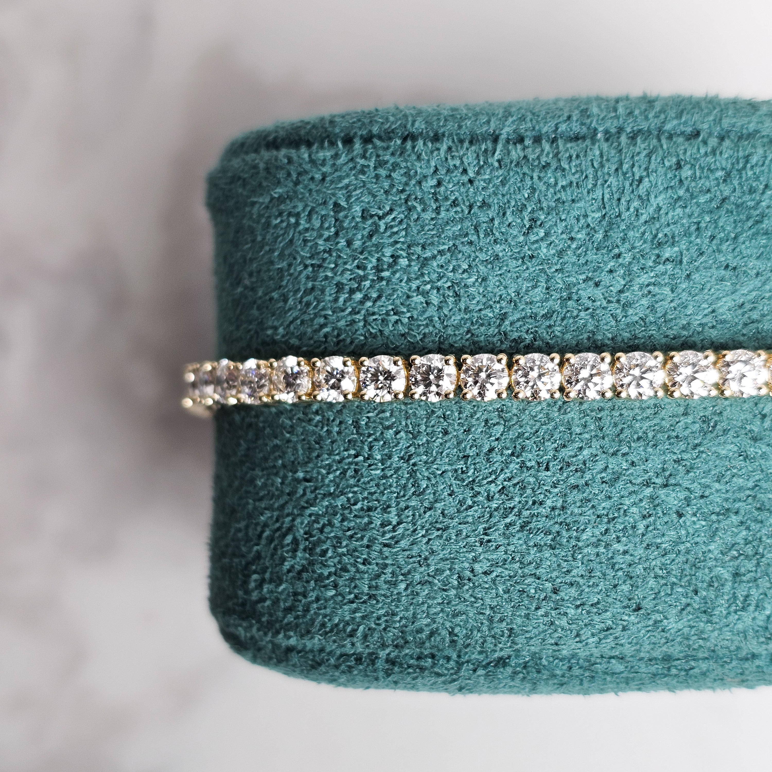 Yellow gold diamond tennis bracelet on marble background and green velvet jewellery display 