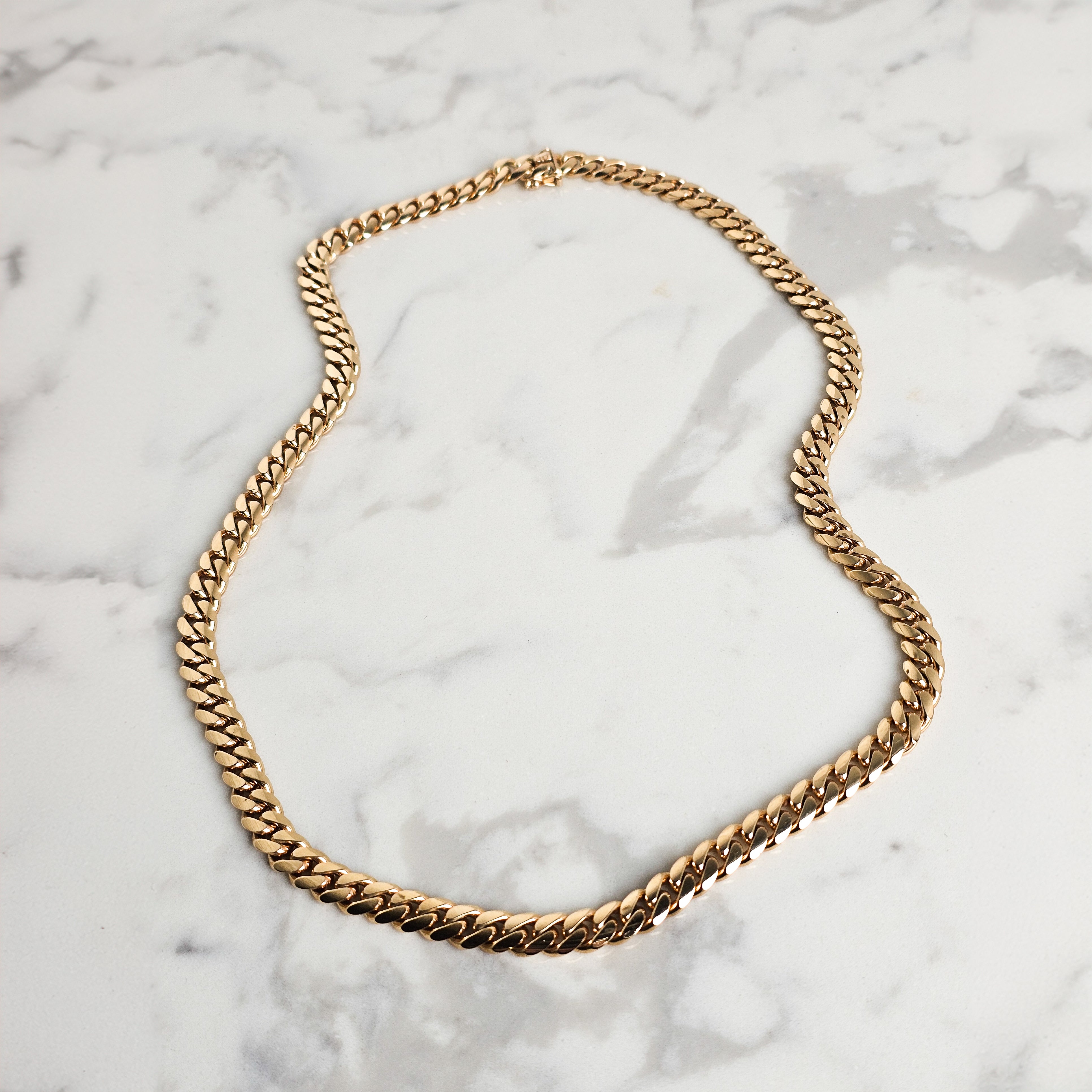 Yellow gold cuban chain on marble background