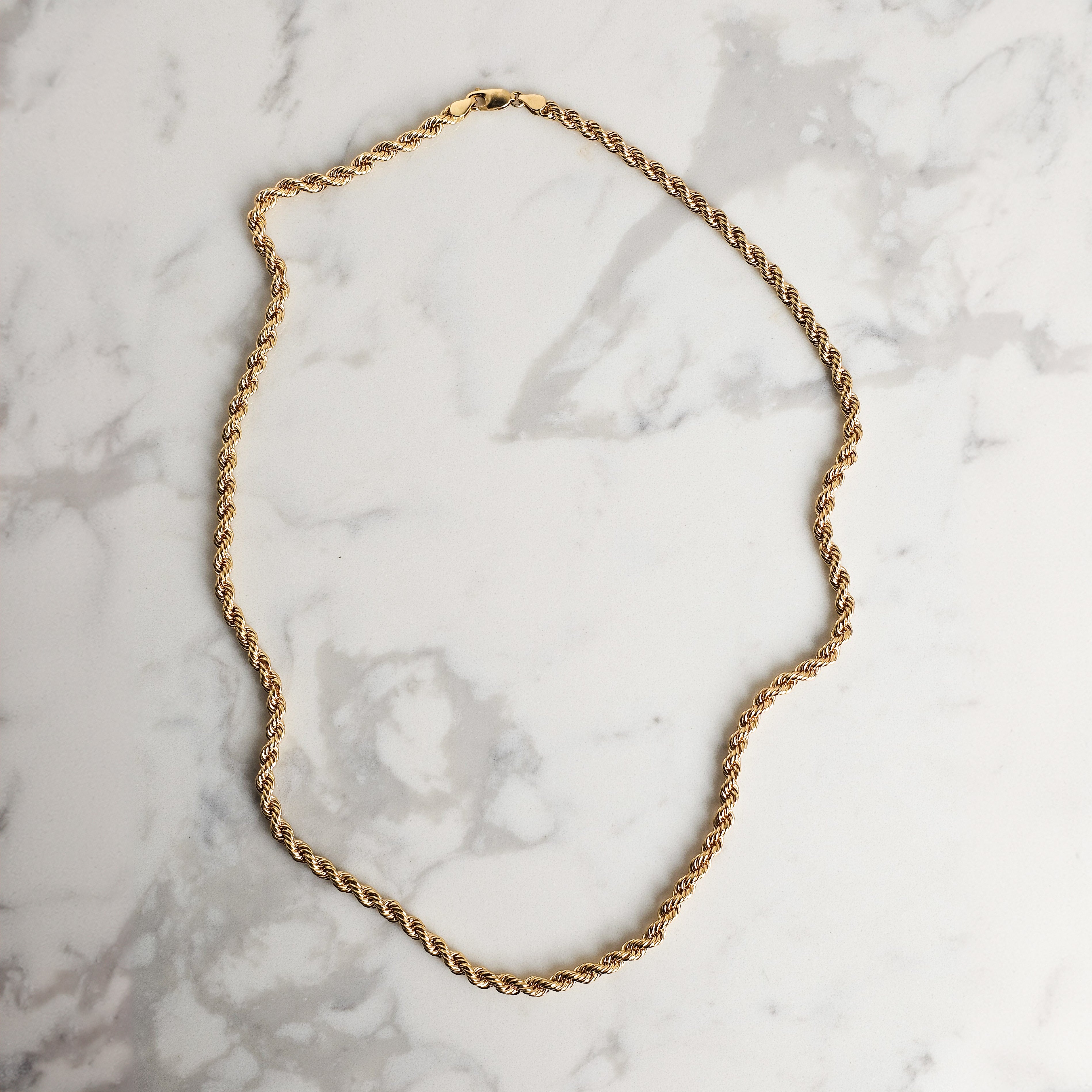 mens rope chain in yellow gold on marble background artfully displayed 