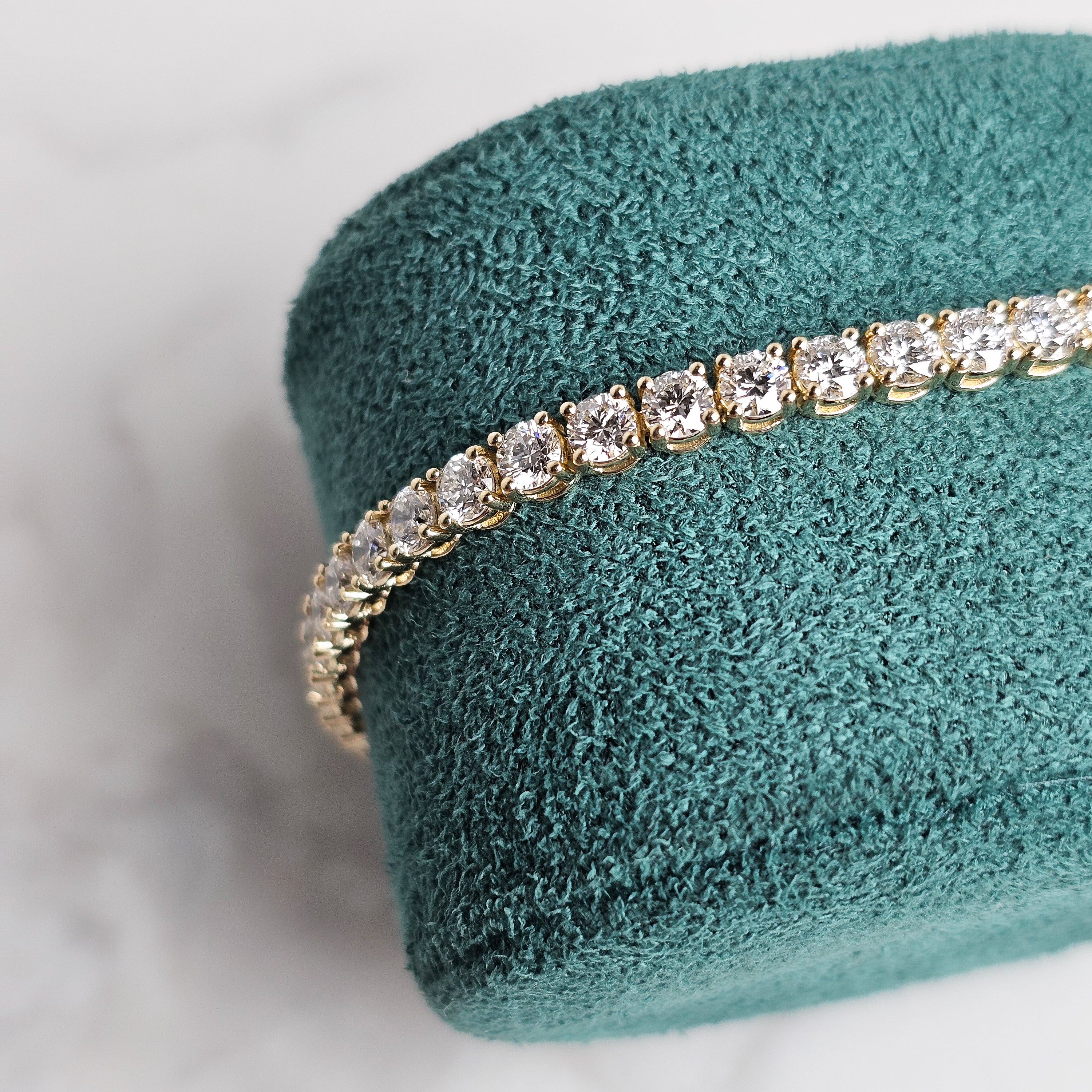 Yellow gold diamond tennis bracelet on marble background and green velvet jewellery display close up